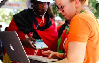 A photo of ProLife Europe member Miriam wearing an orange t-shirt and holding a laptop, with which she shows something on the screen to an interested man