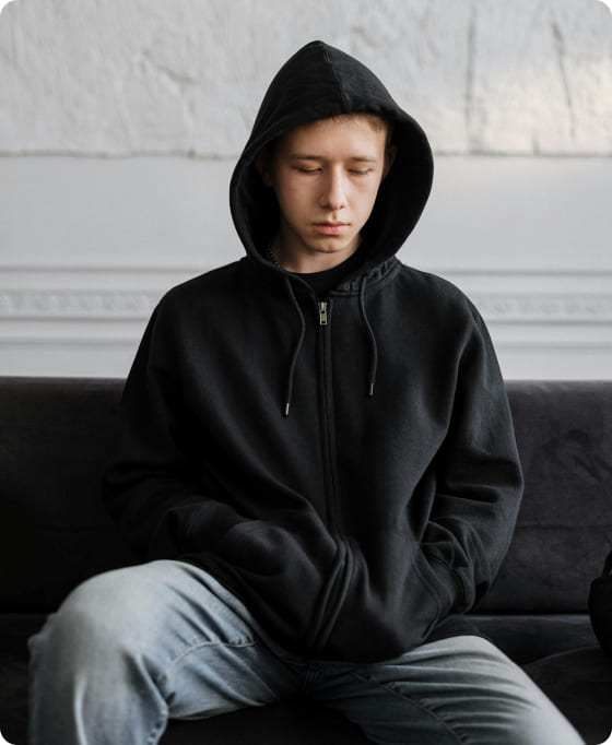 Photo of a young adolescent looking down at the floor, wearing a black hoodie