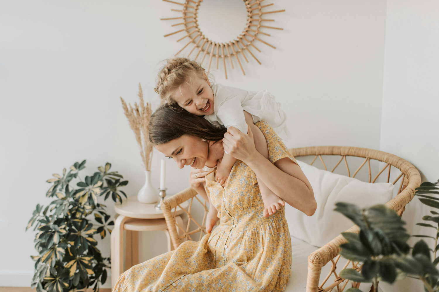 A laughing mother holding her young daughter on her shoulders in an indoors home environment