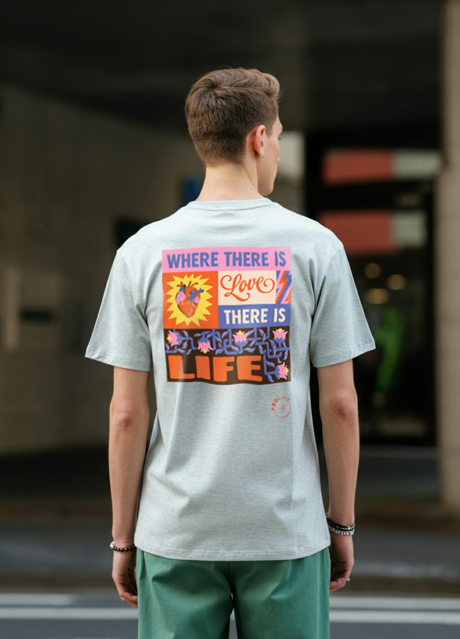 A man wearing the grey t-shirt from the ProLife Europe merchandise collection, facing away from the camera and wearing green trousers in an urban setting